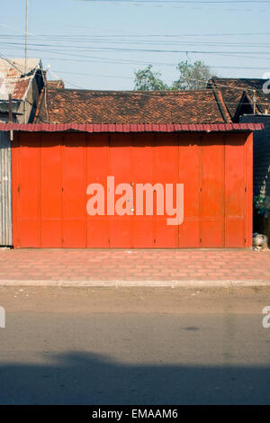 A bright red metal door stands padlocked on a city street in Kampong Cham, Cambodia. Stock Photo