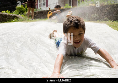 Seven year old boy plays on a homemade slip and slide in his backyard Stock Photo