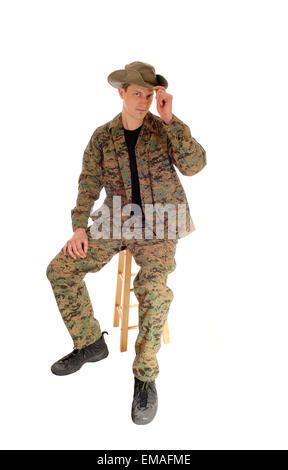 A young soldier sitting on a chair in camouflage uniform and a hat,  isolated for white background. Stock Photo