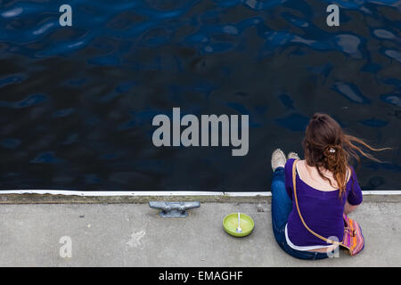 Young woman eating lunch while sitting on a floating dock at Granville Island, Vancouver Stock Photo