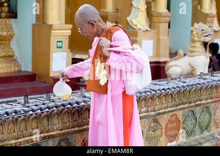 YANGON, MYANMAR - JANUARY 29 :  A buddhist nun pours oil in receptacle for oil lamp at Shwedagon temple Jan 29, 2010, Myanmar to Stock Photo