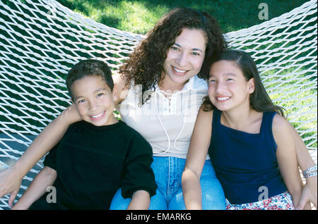 Portrait of mother and two children sitting on backyard hammock Stock Photo