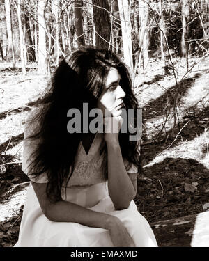 Latina teen sitting on a log in the woods looking thoughtful Stock Photo