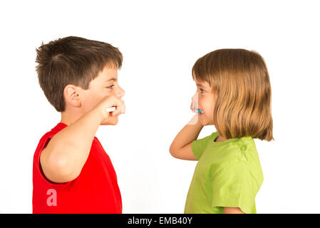 Portrait of a little girl and a young boy brushing teeth facing each other Stock Photo