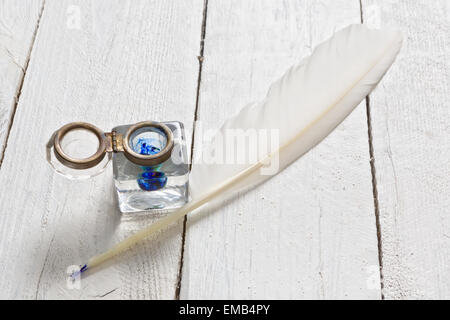 Feather quill and blue ink pot on a rustic white painted table Stock Photo