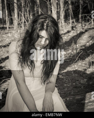 Latina teen sitting on a log in the woods looking lonely, thoughtful, or sad Stock Photo