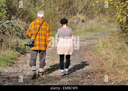 Old wise couple walking and hiking in the country on a footpath during autumn. These walkers are enjoying sports outside. Stock Photo