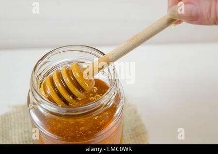 Honey dripping into a glass jar from a special wooden spoon Stock Photo