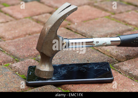Broken mobile phone hit by hammer, lying on the pavement Stock Photo