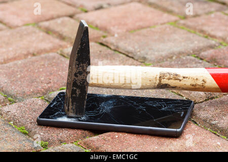 Broken mobile phone hit by hammer, lying on the pavement Stock Photo