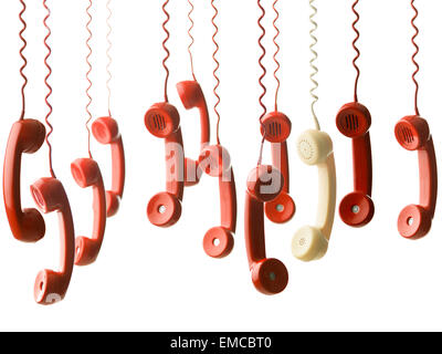 one yellow handset in between many red handsets from vintage phones, hanging against white background Stock Photo