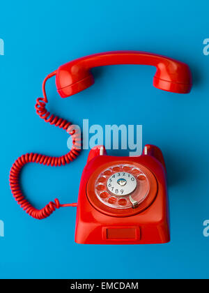 red vintage phone with handset off the hook, on blue background Stock Photo