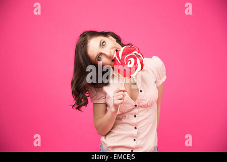 Young beautiful woman bitting lollipop over pink background Stock Photo