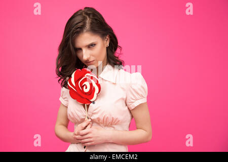 Young woman holding lollipop over pink background. Wearing in shirt. Looking at camera Stock Photo