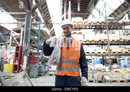 Smiling warehouseman in storehouse carrying tubes Stock Photo