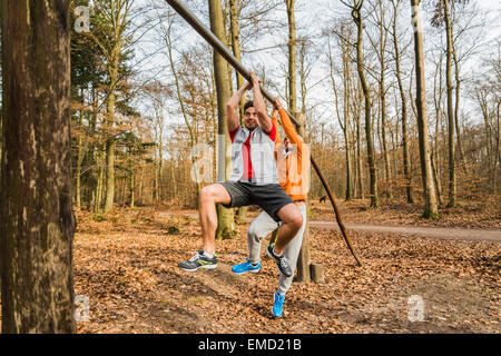 Two young men brachiating on bar in forest Stock Photo