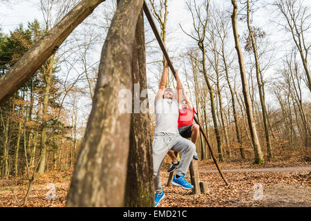 Two young men brachiating on bar in forest Stock Photo