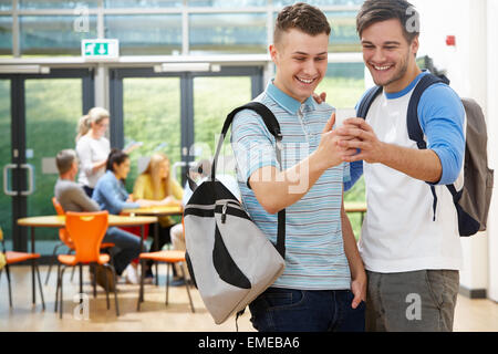 Two Male Students In Classroom Reading Message On Phone Stock Photo