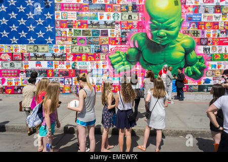 Passer-by admire the new mural by renowned street artist Ron English on the new Bowery Mural in Soho in New York on Saturday, April 18, 2015. English's work parodies and criticizes consumerism and it is his first public work in over a year. The reconstructed space, curated by Jeffrey Deitch, is famous for hosting murals by graffiti artists, most notably Keith Haring . (© Richard B. Levine) Stock Photo