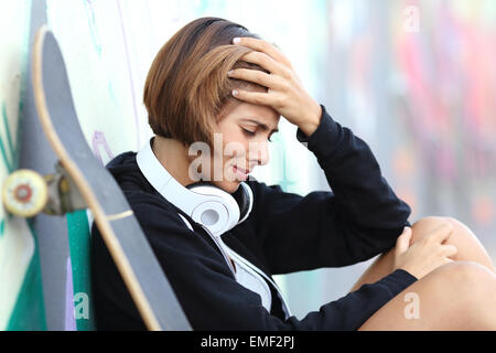 Worried or depressed teenager girl leaning on a wall with blurred graffiti Stock Photo