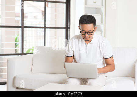 Southeast Asian male using internet at home, sitting on sofa relaxing Stock Photo