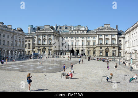 People tourists enjoy fountains & Neoclassical buildings surrounding  cobblestone courtyard spring sunshine at Somerset House Strand London England UK Stock Photo