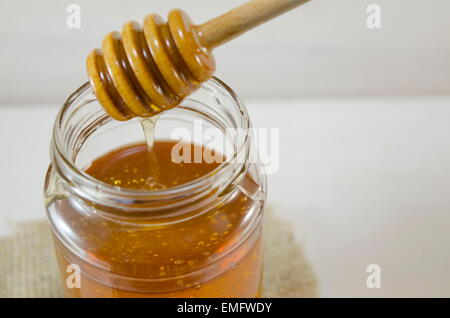 Honey dripping into a glass jar from a special wooden spoon Stock Photo