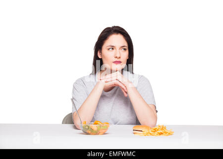 picture of woman with fruits and hamburger in front on white background, healthy versus junk food concept Stock Photo