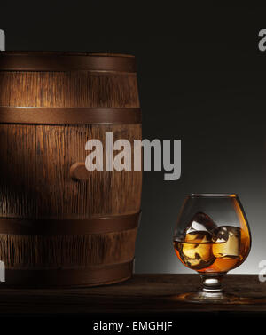 Glass of matured whiskey with ice cubes in it and old wooden barrel. Stock Photo