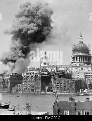 Huge smoke clouds billow from the burning Thameside warehouse after a fire broke out. Flames reached hundreds of feet into the sky and four firemen were reportred trapped inside when an interior staircase collapse. St Pauls Cathedral on the right of the picture is framed in scaffolding for restoration and cleaning. 28th June 1965. Stock Photo