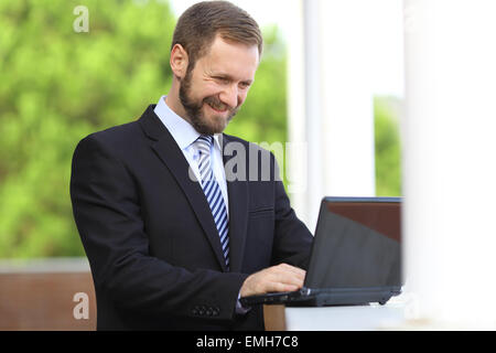Happy business man working browsing internet in a laptop outdoor with a green background Stock Photo