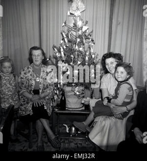 1950s, historical, A happy family xmas. Mum, grandma and two children sit beside a small and simply decorated christmas tree on top of a little side table. Stock Photo