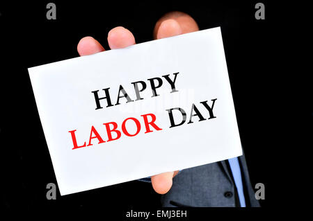 a young caucasian man wearing a grey suit shows a signboard with the text happy labor day written in it, against a black backgro Stock Photo