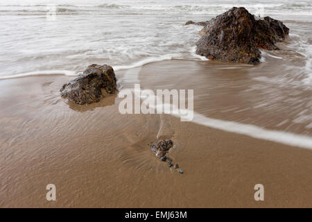 Water rushes around rocks on beach. Stock Photo