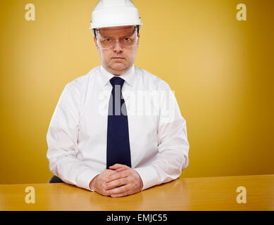 Serious male engineer in office and he looks toward the camera, he wearing a white shirt and blue tie, head he wears a white har Stock Photo