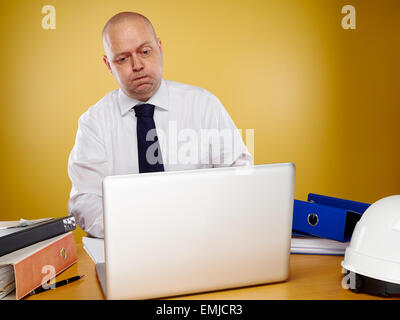 Hardworking male engineer in office, he wearing a white shirt and tie, the laptop, binders and white hard hat is on the table Stock Photo