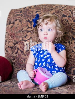A beautiful 14 month old Caucasian girl sits in a chair and eats crackers. USA Stock Photo