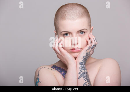 A young woman with a shaved head and tattoos on her shoulder, arms and ...