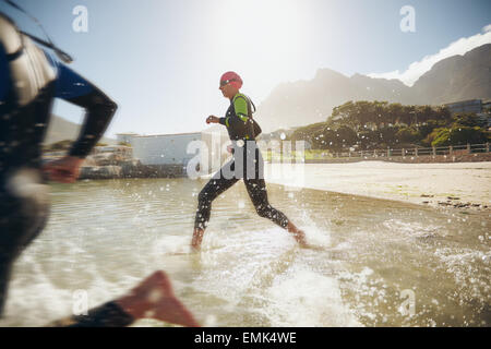 Participants running into the water for start of a triathlon. Two triathletes rushing into water. Stock Photo