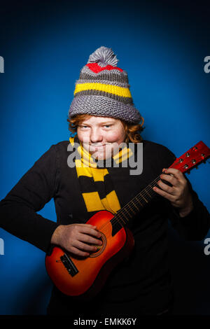 Red-haired expressive teenage boy playing on ukalele, music concept Stock Photo