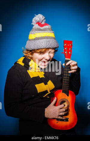 Red-haired expressive teenage boy playing on ukalele, music concept Stock Photo