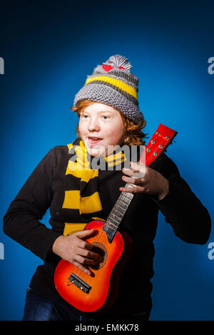 Red-haired expressive teenage boy playing on ukalele, music concept Stock Photo