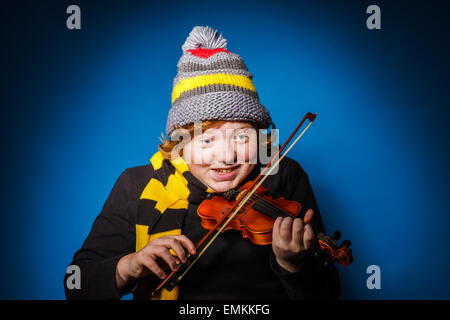 Red-haired expressive teenage boy playing violin, funny concept, isolated on blue Stock Photo