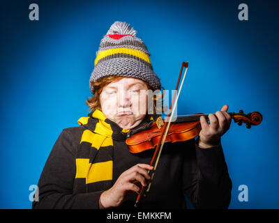 Red-haired expressive teenage boy playing violin, funny concept, isolated on blue Stock Photo