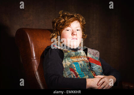 Red-haired expressive teenage boy sitting in arm-chair, studio portrait Stock Photo