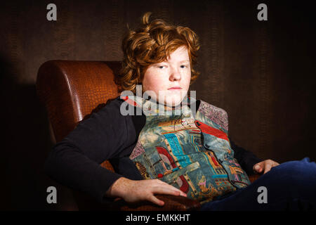 Red-haired expressive teenage boy sitting in arm-chair, studio portrait Stock Photo