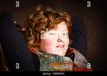 Red-haired expressive teenage boy sitting in arm-chair, studio portrait Stock Photo