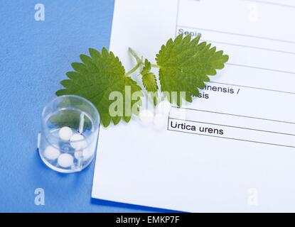 Urica Urens and homeopathic pills in plastic container on homeopathy related sheet Stock Photo