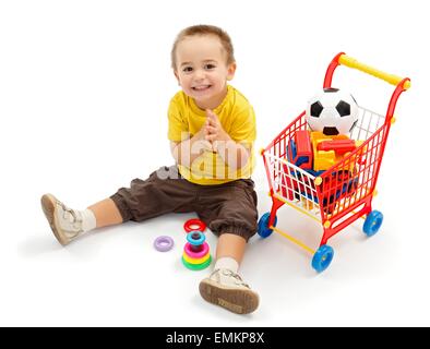 Happy little boy sitting on ground, and playing. New toys in small shopping cart Stock Photo