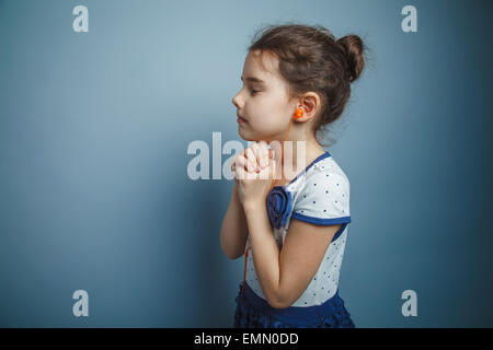 a girl of seven European appearance brunette folded her hands in supplication listening to music with headphones on a gray backg Stock Photo